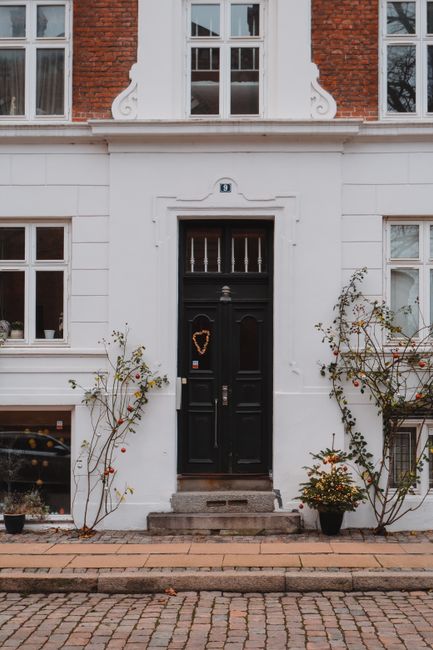 The image shows the front façade of a traditional brick townhouse with white decorative architectural details around the windows and doorway, typical of London terrace housing. The black front door is